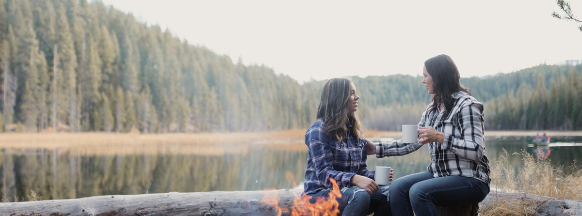 mother and daughter sipping coffee by a fire at the lake