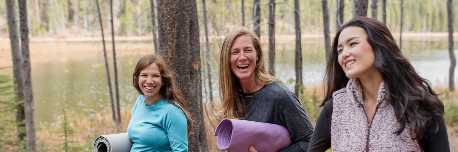 three healthy women walking in the woods with yoga mats