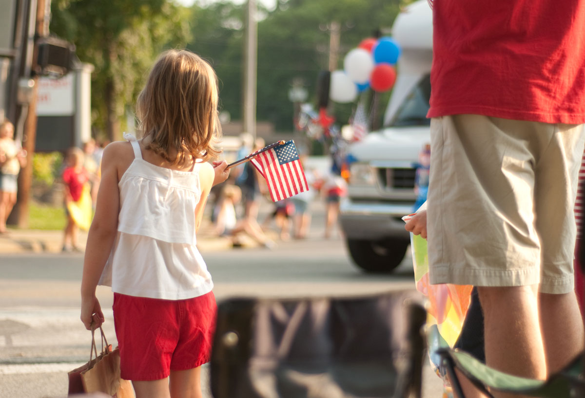 Little girl watching parade with American flag in hand
