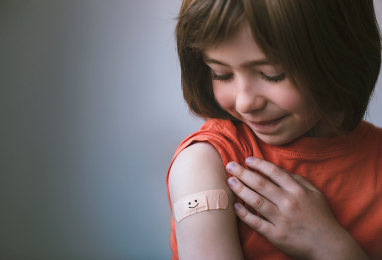 young child looking at vaccination site bandaid with smiley face