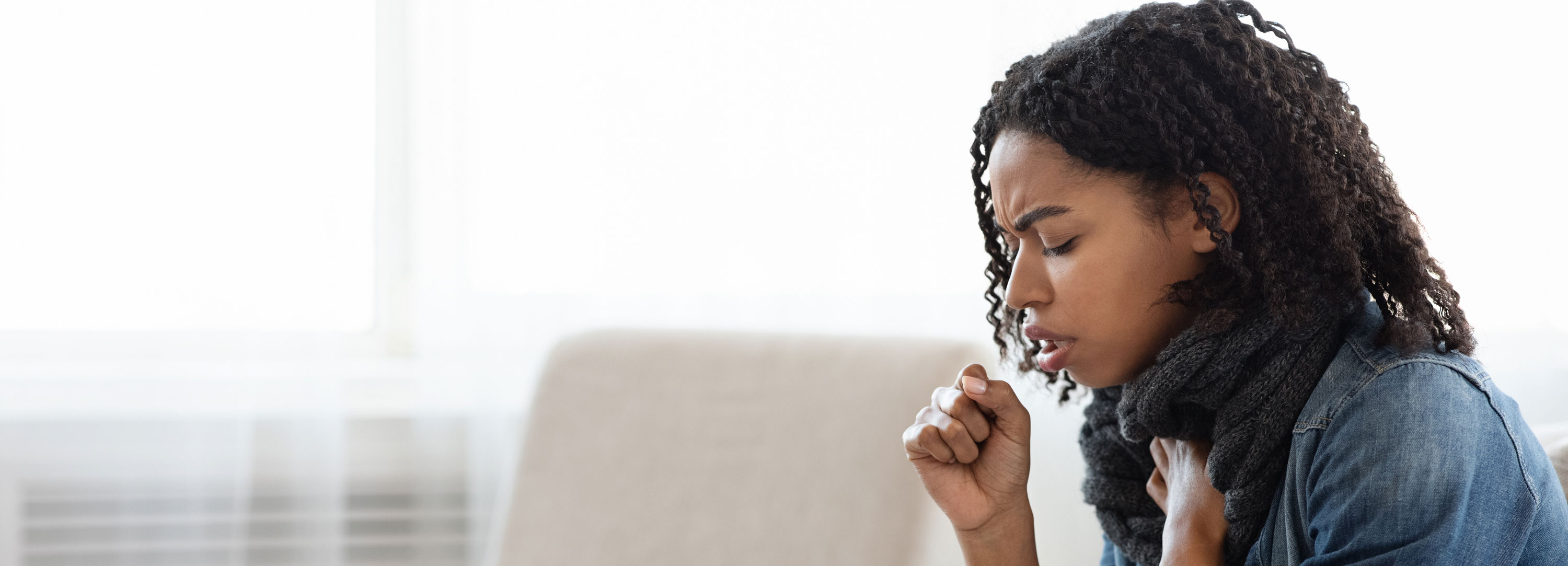 African American woman coughing while sitting on a couch